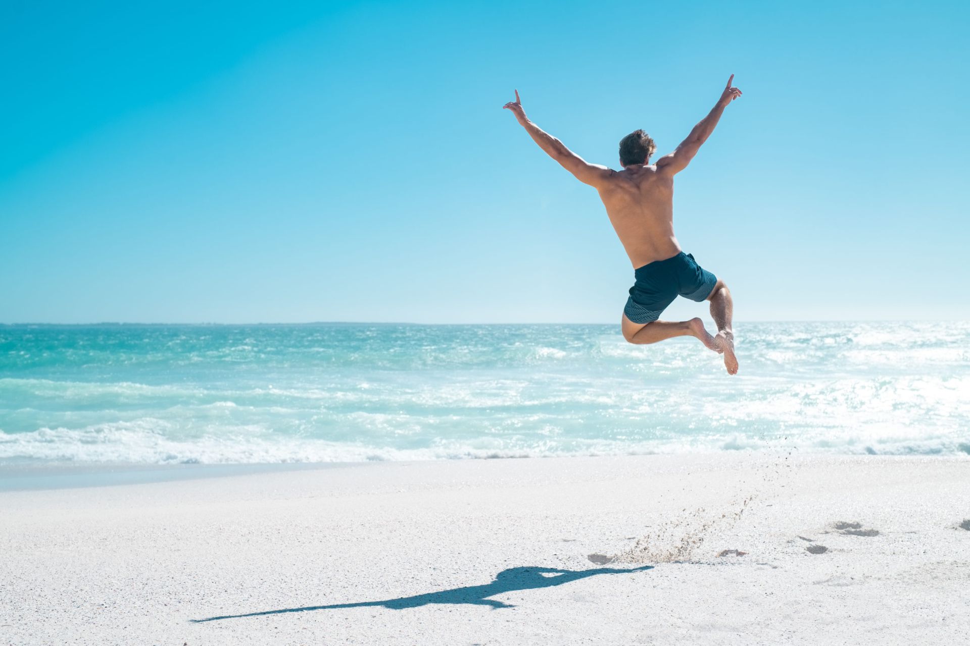 Mann springt am Strand in die Luft