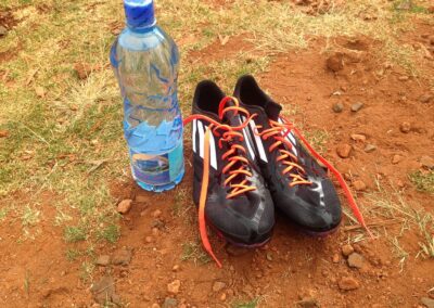 Laufspikes und Wasserflasche auf roter Erde in Iten, Kenia